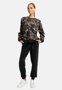 Schwarzer Sweatshirt mit floralem Muster und Rundhalsausschnitt, kombiniert mit schwarzen, zulaufenden Jogginghosen und weißen Sneakers mit strukturierter Sohle.