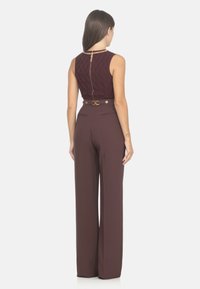 Top burdeos sin mangas con un patrón texturizado, detalle de cremallera dorada, combinado con pantalones de pierna ancha de tiro alto y un cinturón a juego.