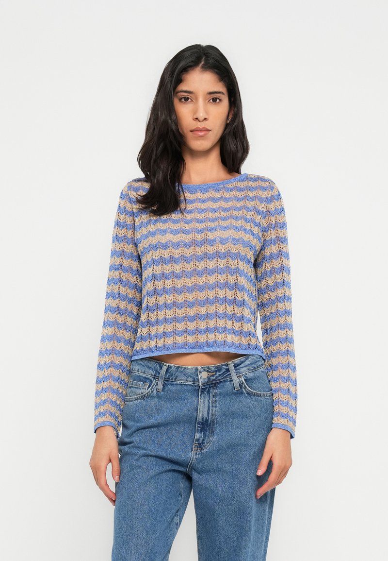 Hosszú ujjú, kivágott pulóver hullámmintával, kék és bézs színekben, kötött textúrával és kerek nyakkivágással. Magas derekú farmerral párosítva.