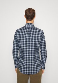 Károvaná košile v námořnické modré, zelené a bílé barvě z bavlny. Obsahuje zadní yoke, manžety na knoflíky a zakřivený lem.