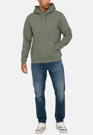 Hooded sweatshirt in olive green, featuring a front pocket, ribbed cuffs, and hem. Paired with blue denim jeans and white sneakers.