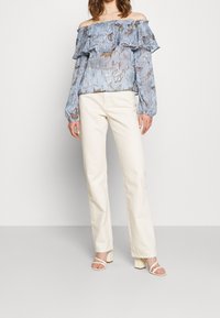 Top azul claro sin hombros con capas con volantes, patrón floral, combinado con pantalones de pierna ancha crema y sandalias de tacón blanco con tiras.