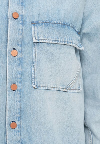 Το ανοιχτό μπλε πουκάμισο jeans διαθέτει κουμπιά από χαλκό, τσέπη στο στήθος, αντίθετη ραφή και χαλαρή εφαρμογή με απαλό ύφασμα.