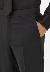 Juodos važinėjimo kelnės su lygia tekstūra, turinčios šoninį kišenių, liekną fasoną ir puikiai išsiuvinėtas siūles.