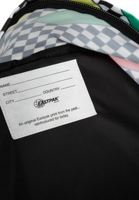 Black backpack interior with multi-colored patterned fabric, including a checkered design. Features a white label for personal information.