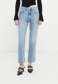 Jeans azzurri a gamba dritta con vita alta, caratterizzati da un classico design a cinque tasche e orlo grezzo, abbinati a scarpe nere con punte appuntite.
