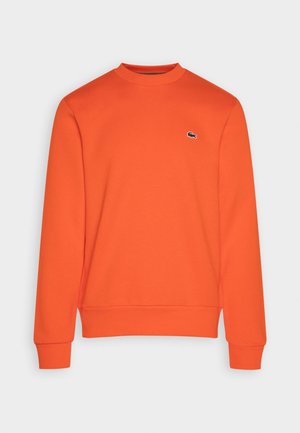 Sweat-shirt orange vif à manches longues et col rond, avec poignets et ourlet côtelés, avec un petit logo crocodile noir et blanc sur la poitrine.