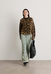 Svetr s leopardím vzorem, světlé zelené kalhoty širokého střihu, černá taška a černé boty. Texturovaný, ležérní design s charakteristickým zvířecím vzorem.