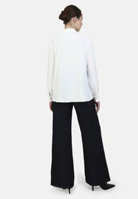 White long-sleeve blouse with a split back detail, paired with wide-leg dark denim pants and black high-heeled shoes.