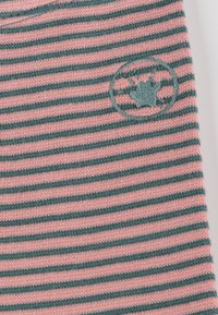 Gestreifter Stoff in Pink und Grün mit einem runden gestickten Logo, das ein Blattdesign zeigt, mit Fokus auf Textur und Farbkontrast.