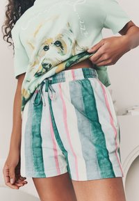 Pārizmēra zaļgani mīksts krekls ar suņa grafiku un uzrakstu "pooped", kombinēts ar svītrainām viegli uzvelkamām šortām zilā, rozā un baltā krāsā.