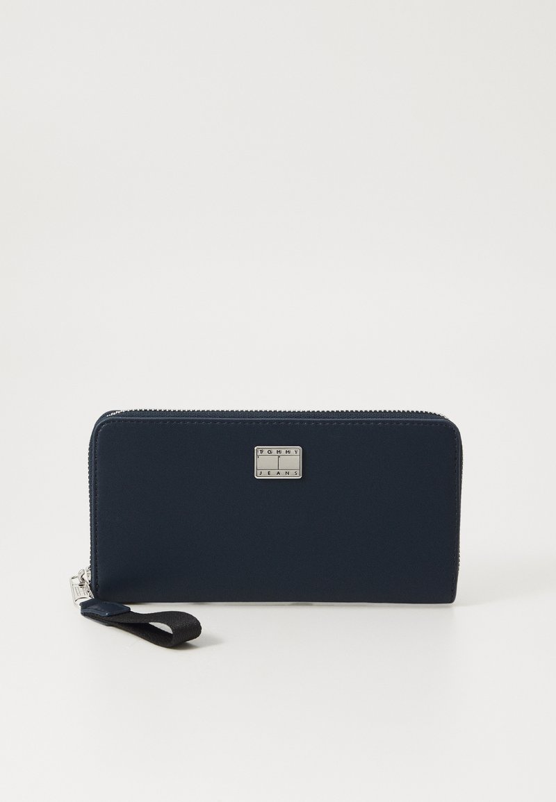 Portafoglio con zip navy realizzato in materiale liscio, dotato di una placca logo in tonalità argento e di un cinturino in tessuto nero per un facile trasporto.