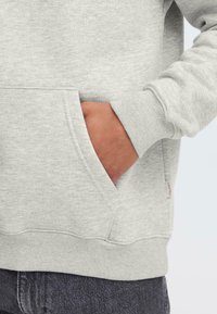 Light gray sweatshirt with a kangaroo pocket, ribbed cuffs, and waistband. Soft material texture, features a small branded label on the side.