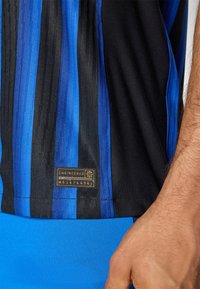 T-shirt de sport rayé noir et bleu avec un design texturé, étiquette en tissu portant "ENGINEERED" et "MB 1474496", manches courtes et matériau évacuant l'humidité.