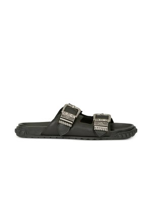 Sort slip-sandal med to brede remme med udsmykkede sølvspænder og en robust tekstureret sål.