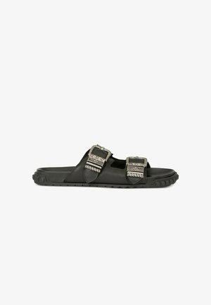 Sort slip-sandal med to brede remme med udsmykkede sølvspænder og en robust tekstureret sål.