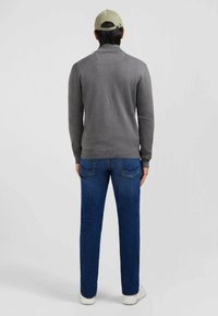 Pull gris à col haut, porté avec un jean bleu et des baskets blanches. Tissu texturé, design ajusté et poignets côtelés.