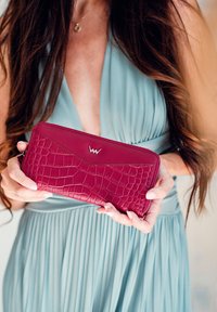 Textured, burgundy wallet featuring a crocodile pattern and a contrasting smooth section. Zipper closure with a prominent logo detail.