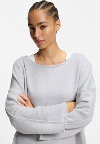 Grauer übergroßer Sweatshirt mit weicher Textur, rohen Kanten am Ausschnitt und langen Ärmeln mit kontrastierenden Nähten.