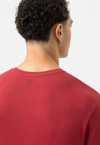 Rotes T-Shirt aus Bio-Baumwolle mit Rundhalsausschnitt, kurzen Ärmeln und einem kleinen aufgedruckten Etikett auf der Rückseite. Glatte Textur.