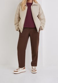 Beige puffer jacket, bordeaux sweatshirt, bruine broek en witte sneakers met bruine accenten. Glad textuur en een ontspannen pasvorm.