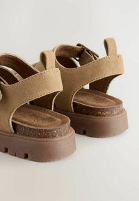 Tanfarbene Wildledersandalen mit verstellbaren Riemen, einem gepolsterten Fußbett und einer klobigen braunen Sohle mit Dämpfung. Einfaches Design mit abgerundeten Kanten.