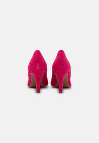 Chaussures à talons hauts en daim rose vif vues de dos, mettant en valeur des talons fins et une texture lisse sur un fond blanc uni.