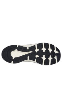 Semelle de chaussure de sport noire et ivoire avec une surface en caoutchouc texturé, un motif de semelle distinct et un logo partiellement visible.