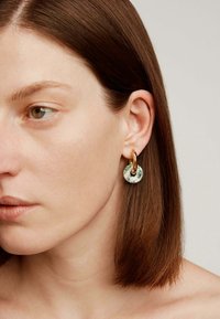 Pendiente circular de mármol verde y blanco con cierre de metal dorado, que presenta una superficie lisa y un diseño minimalista.