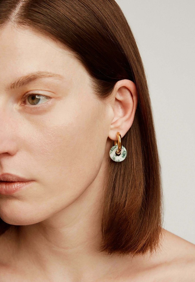 Pendiente circular de mármol verde y blanco con cierre de metal dorado, que presenta una superficie lisa y un diseño minimalista.