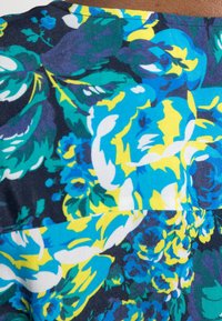 Stoff mit floralem Muster, das große blaue, gelbe und grüne Blumen auf einem dunklen Marinehintergrund zeigt, mit sichtbaren Nähdetails.