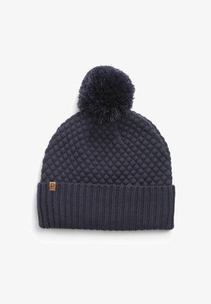 Marineblauwe gebreide muts met een gestructureerd lijf, geribbelde boord en een fluffy pompon bovenop. Verfraaid met een klein bruin label.