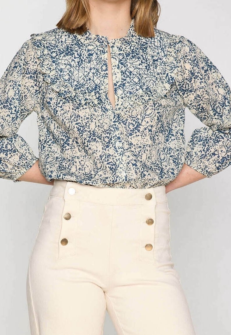 Blommig blus i krämfärgad och marinblå med volangkrage och ett framstående nyckelhål. Matchad med högmidjade kremsvarta byxor med guldfärgad knappdetalj.