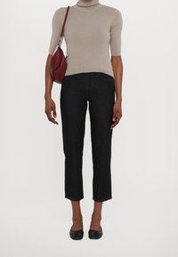 Camiseta de cuello alto ajustada beige, jeans negros recortados y zapatos planos negros. Un bolso borgoña cuelga del hombro. Diseño sencillo, textura suave.