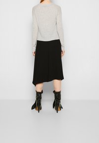 Grauer gestrickter Pullover kombiniert mit einem schwarzen plissierten Midirock. Schwarze Stiefeletten mit gefaltetem Design und spitzen Absätzen setzen kontrastierende Akzente.