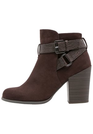 Bottine en suède marron avec une sangle en cuir texturé et un détail de boucle. Bout arrondi et un talon empilé et nervuré.