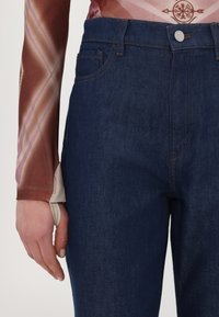 Jeans en denim bleu foncé au design ajusté, dotés d'une fermeture à boutons et à glissière à l'avant, de passants de ceinture et de détails de couture subtils.