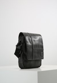 Borsa messenger in pelle nera con chiusura a patta, tracolla regolabile e tasca frontale. Texture liscia e design minimalista.
