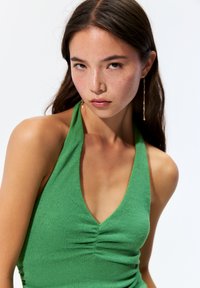 Grünes Neckholder-Top aus strukturiertem Stoff mit tiefem V-Ausschnitt und gerafftem Detail an der Brust.