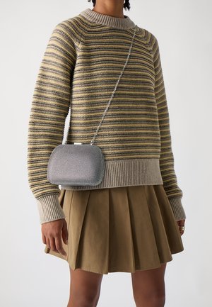 Pull rayé beige et gris avec un col rond, associé à une jupe plissée kaki. Petit sac à main en métal argenté avec une bandoulière chaîne.