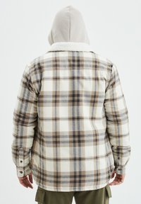 Camicia di flanella a quadri nei colori crema, marrone e grigio con colletto Sherpa. Presenta maniche lunghe e polsini con bottoni. Tessuto morbido con motivo a quadretti.
