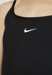 Svart ribbat linne med rundad halsringning och tunna axelremmar. Har en liten vit Nike-logotyp på framsidan.