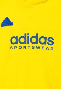 Sudadera amarilla con un gran logo azul de "adidas" y el texto "SPORTSWEAR". Tejido suave con un bolsillo frontal y capucha ajustable.