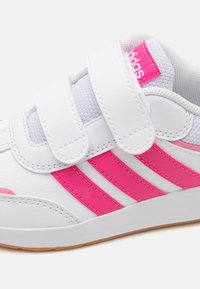 Białe buty sportowe z różowymi akcentami, z trzema różowymi paskami, zapięciem na rzepy i teksturowanym językiem z siateczki dla lepszej wentylacji.