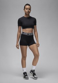 Svart cropped treningsgenser, høyt midjebånd svart shorts med logo, sporty svarte og hvite sko. Glatte materialer med figursydd design.
