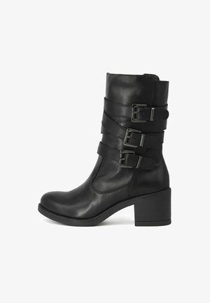 Stivale alla caviglia in pelle nera con tre cinturini regolabili con fibbie, punta arrotondata e tacco chunky di 7 cm. Texture liscia e dettagli di cucitura minimali.