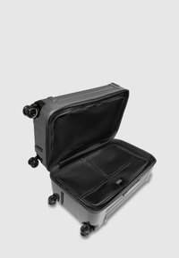 Hartschalenkoffer in Grau mit offenem schwarzem Innenraum, ausgestattet mit vier Rollen, Reißverschlussfächern und strukturierter Oberfläche.