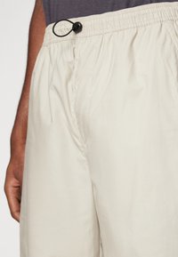 Shorts de color beige claro, fabricados en un tejido suave, que presentan una cinturilla elástica con ajuste mediante cordón y costuras frontales visibles.