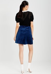 Haut en tricot noir à rayures avec des manches bouffantes associé à une jupe bleu marine longueur genoux. Des bottines blanches à la cheville complètent la tenue.