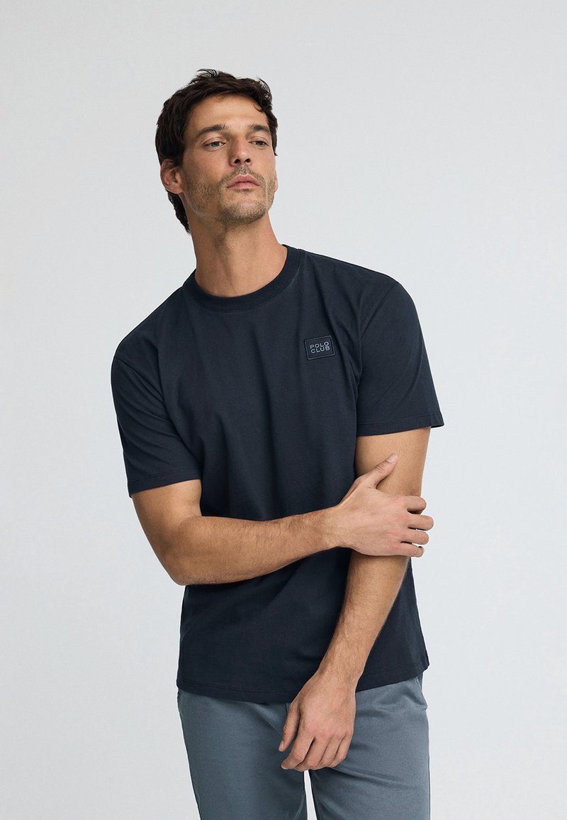 Schwarz, kurzärmliges T-Shirt aus Baumwolle mit einem strukturierten quadratischen Patch und dem Schriftzug "POLO CLUB" auf der linken Brust. Glatte Stoffqualität.